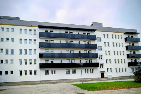 Nowoczesny budynek sanatorium uzdrowiskowego z białymi ścianami i czarnymi balkonami. W tle błękitne niebo.