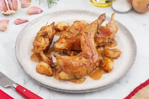 Plato de conejo al ajillo con trozos de ajo y romero. Una delicia para aprender cómo hacer conejo al ajillo.