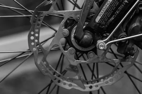 Zbliżenie na tarczę hamulcową i szprychy roweru. Widoczny mechanizm szybkiego zwalniania Shimano i ostrzeżenie. RWD.