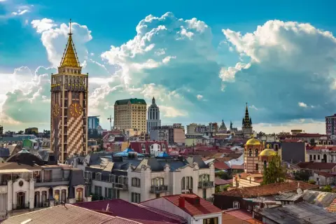 Widok na stolicę Adżarii, Batumi, z charakterystyczną wieżą zegarową i złotymi kopułami cerkwi pod błękitnym, chmurnym niebem.