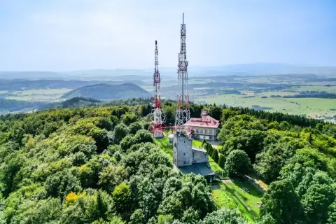 Wieże telekomunikacyjne na zalesionym szczycie Chełmiec. W tle rozległa panorama krajobrazu.