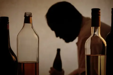 Flera flaskor alkohol framför en person i silhuett. Bilden illustrerar utmaningar med alkohol och arbetsgivarens rehabiliteringsansvar.