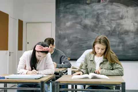 Uczniowie skupieni na zadaniach. Dziewczyna pisze, druga czyta. W tle tablica. Kiedy skończą, będą wiedzieć, jak budowa future perfect simple.