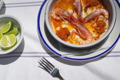 Un plato de gambas en salsa, preparado por un chef del mar, con gajos de lima al lado.