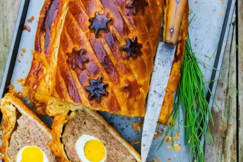 Pâté de Pâques doré, décoré d'étoiles, avec des œufs entiers au cœur. Une recette festive prête à être dégustée.