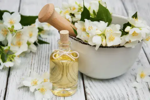 Jasminöl in einer Flasche, umgeben von Blüten. Die Jasmin Wirkung auf die Psyche ist beruhigend und stimmungsaufhellend.