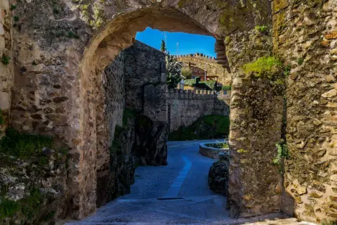Un pasaje de piedra antigua nos lleva a descubrir lugares secretos de la Sierra de Madrid, con un camino empedrado y murallas que evocan historia.