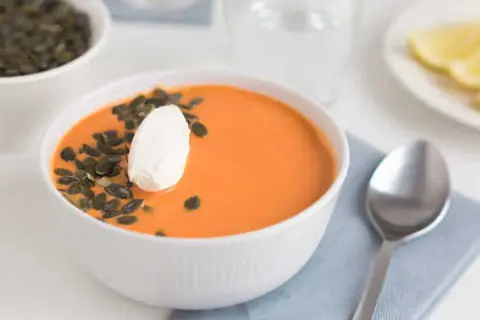 En skål med krämig linssoppa med potatis, toppad med en klick gräddfil och pumpafrön. En sked ligger bredvid.