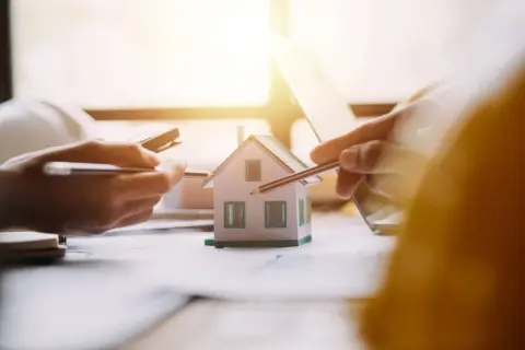 Mani che studiano un modello di casa, con matite e calcolatrice. Si discute il surroga mutuo significato per un nuovo acquisto immobiliare.