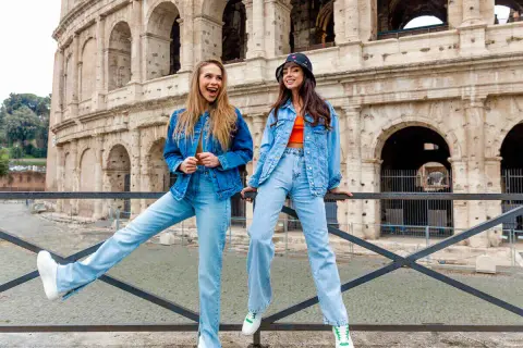 Dwie kobiety w strojach w kolorze denim pozują przed Koloseum. Jedna ma rozpuszczone włosy, druga nosi kapelusz.