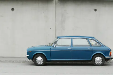 Blå Austin Maxi parkerad vid en betongvägg. En klassisk bil som väcker minnen.