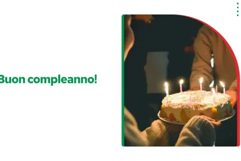 Tort urodzinowy z zapalonymi świeczkami, ktoś trzyma go w rękach. Napis "Buon compleanno!" życzy wszystkiego najlepszego sto lat po włosku.