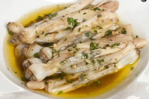 Navajas a la plancha con ajo y perejil, servidas en un plato blanco con aceite dorado.