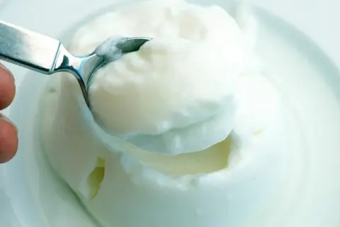 Cremiger Joghurt, eine köstliche Alternative zu saurer Sahne, wird mit einem Löffel aus einer Schüssel gehoben.