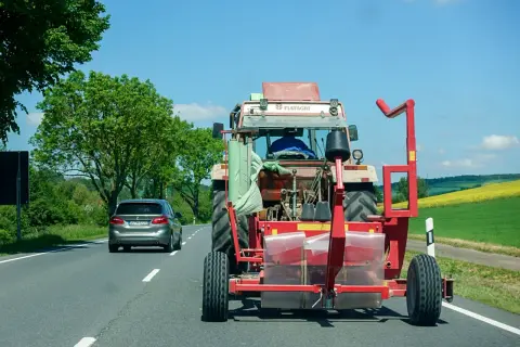 Ein Traktor mit Ballenwickler fährt langsam auf der Autobahn. Ein Auto dahinter gibt Lichthupe, um zu überholen.