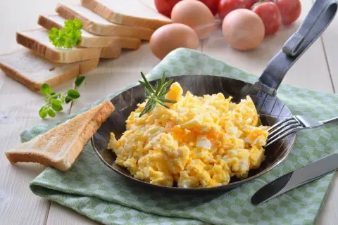 Puszysta jajecznica z proszku, podana na patelni z gałązką rozmarynu, obok tostów i pomidorów.
