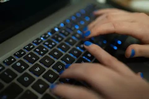 Dłonie z niebieskim lakierem na paznokciach piszą na podświetlanej klawiaturze MacBooka. Twarda spacja jest widoczna.