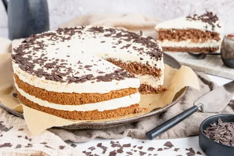 Eine köstliche Cappuccino Torte mit Schokoladenraspeln bestreut, auf einem Teller mit einem angeschnittenen Stück.