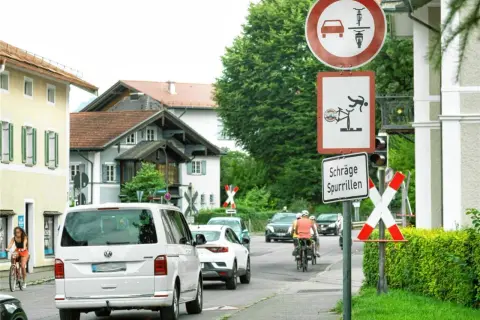 Verkehrszeichen 277 weist auf schräge Spurrillen hin. Ein Radfahrer wird gezeigt, der fast stürzt. Autos und Radfahrer fahren auf einer Straße.