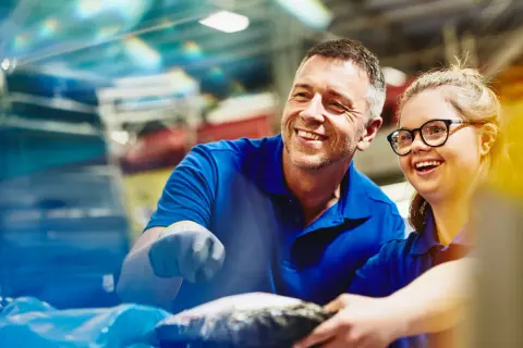Un uomo e una donna sorridono mentre lavorano insieme. Un esempio di inclusione e pari opportunità, anche per le ferie categorie protette.