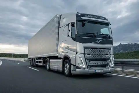 Un tracteur Volvo FH Globetrotter tracte une semi-remorque sur une autoroute. La longueur impressionnante de l'ensemble est mise en valeur par le paysage montagneux en arrière-plan.