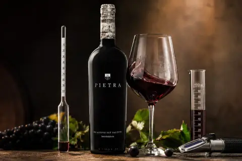 Butelka wina Pietra, kielich z czerwonym winem, winogrona i przyrządy do pomiaru alkoholu. To wino 18 procent, idealne do degustacji.