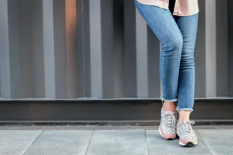 Nogawki dżinsów postrzępione na dole, modny trend. Stylowe sneakersy z błyszczącymi detalami.
