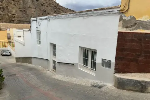 Calle empedrada en un pueblo blanco de Andalucía, con casas encaladas y una ladera rocosa al fondo. Un coche plateado aparcado. Gador, Almería.