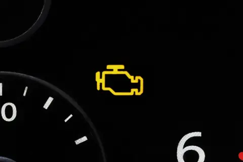 Gelbes Motorzeichen leuchtet auf dem Armaturenbrett eines Autos auf. Es ist Zeit, die Werkstatt zu besuchen.