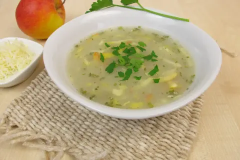 Aromaticzna zupa chrzanowa z chrzanem ze słoika, udekorowana natką pietruszki, obok jabłko i starty ser.