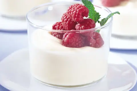 En len vit chokladmousse toppas med färska hallon och en myntakvist i ett glas.