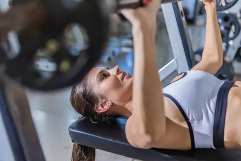 Kvinna utför incline press med skivstång på ett gym.