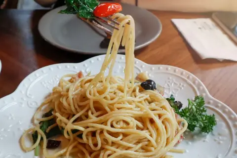 Widok z bliska na talerz pysznego spaghetti aglio olio, z widelcem unoszącym porcję makaronu, listkami bazylii i pomidorkiem.