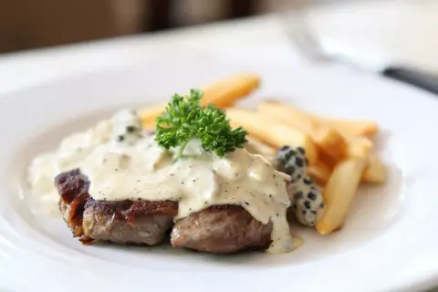 Filete de res bañado en cremosa salsa a la pimienta, acompañado de papas fritas y perejil fresco.