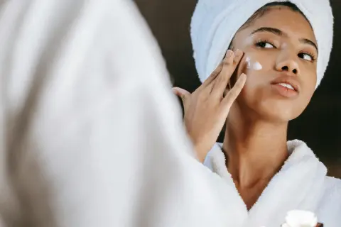 Frau mit Handtuch auf dem Kopf trägt Creme auf, die Glykolsäure und Niacinamid enthält.