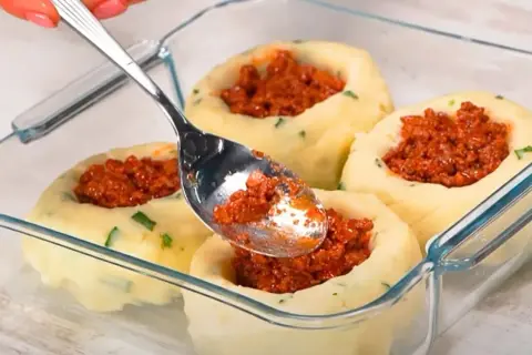 Łyżka nakłada mięsny farsz do ziemniaczanych babeczek. Idealny obiad na dwa dni, gotowy do zapieczenia.
