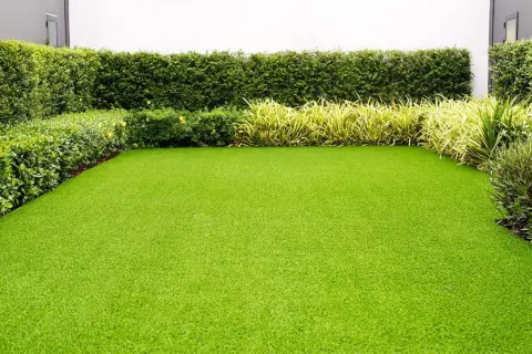 Un jardín impecable con césped artificial verde vibrante, rodeado de setos y plantas. Ideal para quienes buscan cual es el mejor césped artificial para jardín.