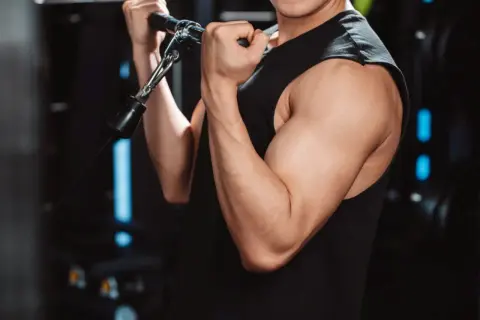 Mięśnie bicepsa mężczyzny ćwiczącego na siłowni. Cytrulina co daje? Poprawia przepływ krwi, co może wspierać trening.