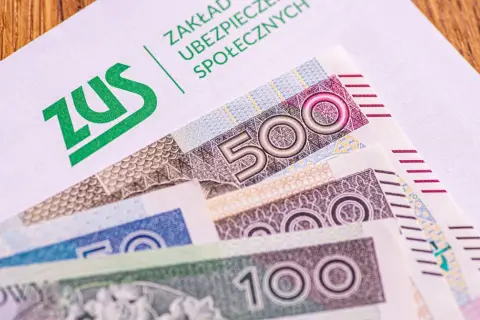 ZUS na białej kopercie, pod nią polskie banknoty 500, 200 i 100 zł. Czekamy na 14. emeryturę.