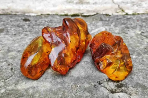 Tre pezzi di ambra baltica grezza, luminosi e traslucidi, mostrano le loro affascinanti proprietà naturali su una superficie rocciosa.