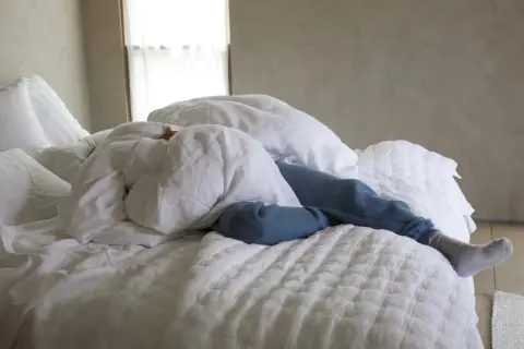 A person sleeps under white linen sheets, a cozy scene that hints at how to wash linen sheets for ultimate comfort.