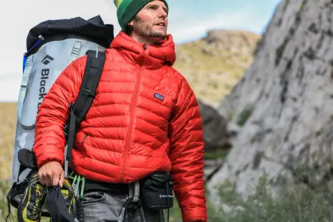 Escaladeur portant une veste rouge en matière doudoune, sac à dos et chaussures d'escalade.