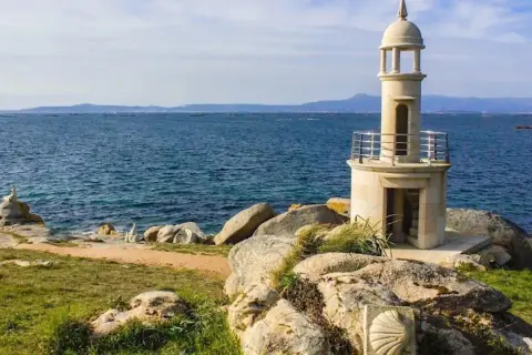 Faro de piedra en Punta Moreiras, con el mar azul de fondo y rocas en primer plano.