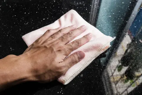 Mano limpiando una superficie de mármol negro con un paño rosa.