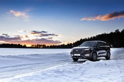 Un SUV noir roule sur une route enneigée au coucher du soleil. La loi montagne impose des équipements pour affronter ces conditions.