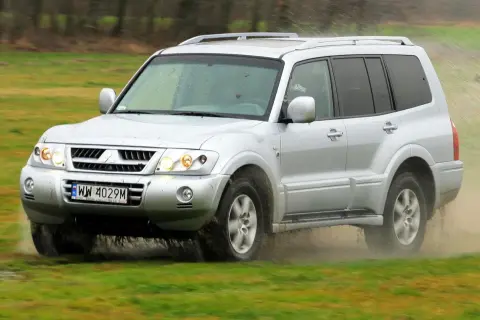 Srebrny Mitsubishi Pajero 3 pokonuje błotniste rozlewiska, unosząc chmury kurzu i wody.