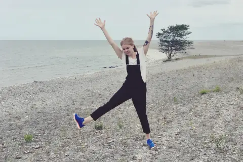 Glad tjej med armarna uppe på en stenig strand på Gotland i Sverige.