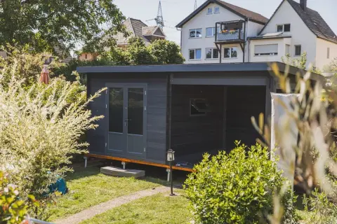 Modernes Gartenhaus mit Doppeltür und überdachter Veranda, ideal als Teil einer bauanleitung gartenhaus. Umgeben von üppigem Grün.