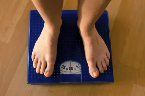Füße auf einer blauen Waage. Die Anzeige zeigt etwa 80 kg. Muskeln sind schwerer als Fett, aber die Waage zählt beides.
