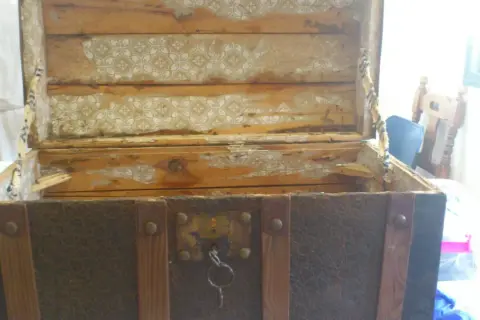 Un baúl antiguo, con su forro despegado y madera desgastada, listo para restaurar.